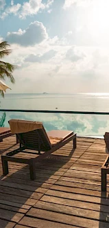 Lounge chairs and umbrellas by a pool with a serene ocean view under a blue sky and scattered clouds.