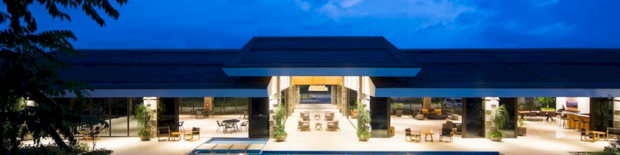 The image shows a luxurious, lit-up pool outside a modern building under a twilight sky, creating a serene atmosphere.