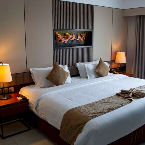 A well-lit hotel room with a large bed, adorned with brown pillows and a decorative runner, flanked by two bedside lamps.