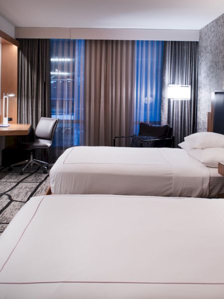 A modern hotel room with two beds, a large TV, desk, and lamps, featuring sleek decor and a patterned carpet.