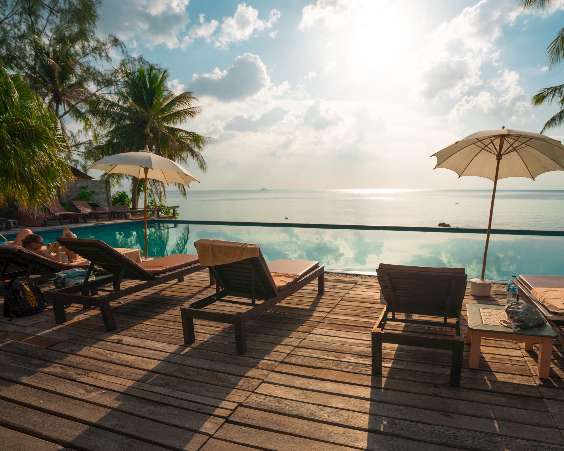 A serene beachfront with deck chairs, umbrellas, and a calm sea under a partly cloudy sky.