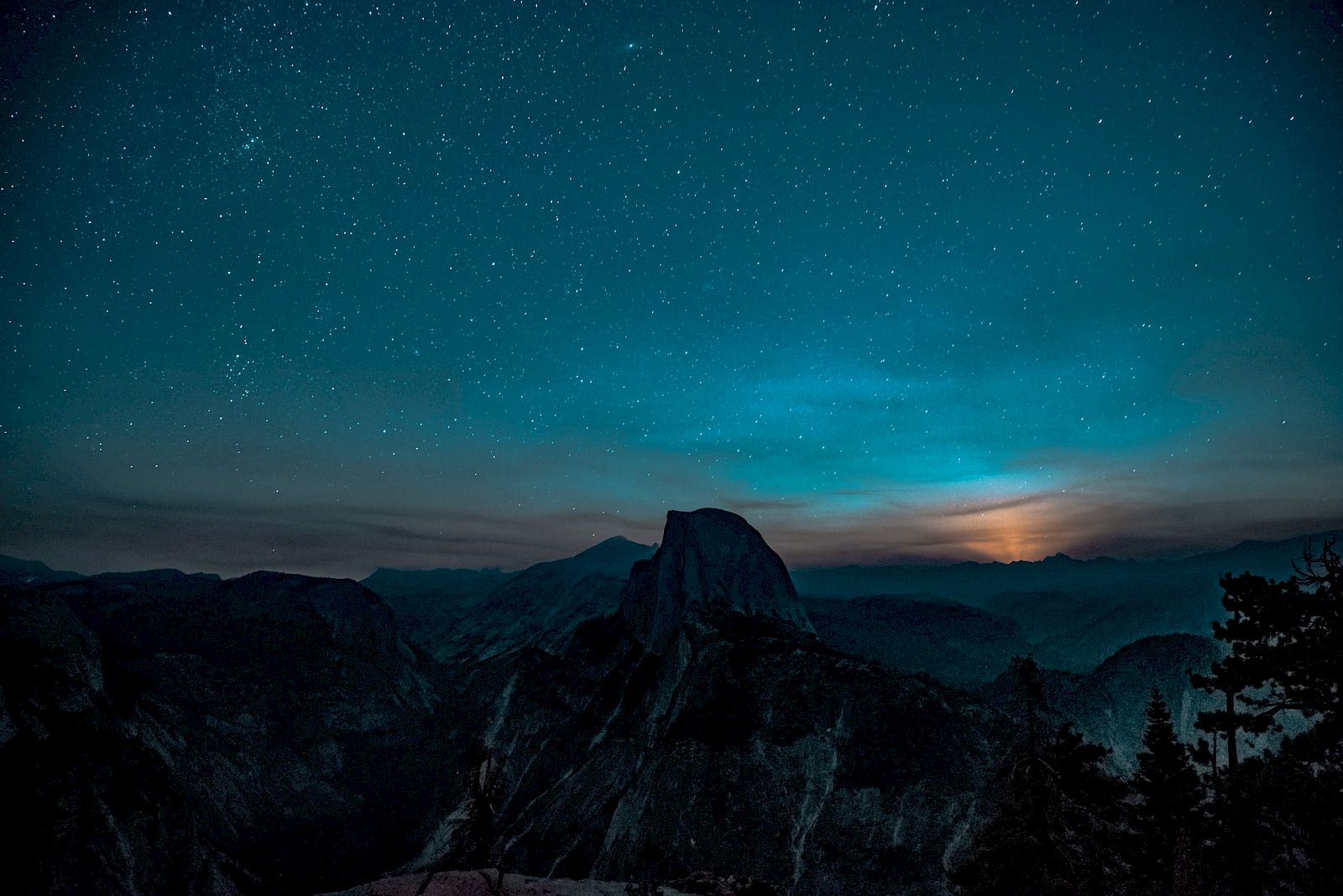 A starry night sky over a mountain range with a visible lunar glow near the horizon creates a serene and picturesque scene.