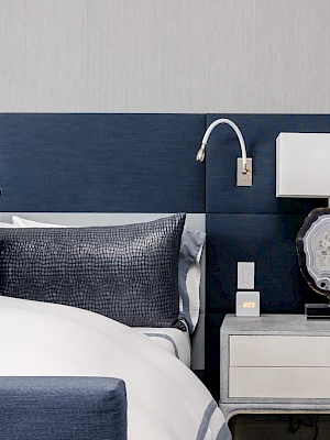A modern bedroom featuring a bed with navy and gray pillows, a lamp on a bedside table, and a sleek, minimalist design.