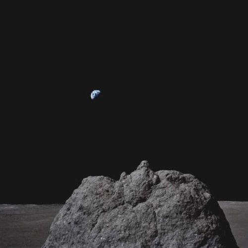 A view from the lunar surface showing a large rock and Earth in the distance against a dark sky.