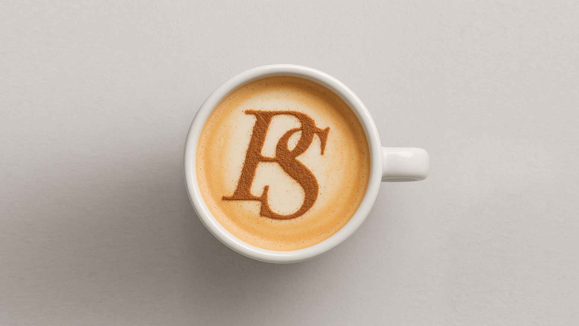 A cup of coffee on a table with latte art forming the letter &ldquo;R&rdquo; at the center of the foam.