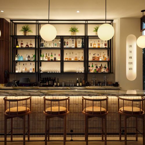 Bar counter with stools, backlit shelves of liquor, warm pendant lights, and a cozy modern dining vibe, perfect for cocktails and conversation.