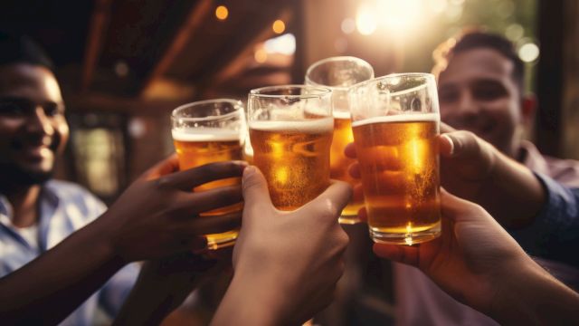 A group of people clinking glasses of beer in a celebratory toast, with warm lighting and a festive atmosphere.