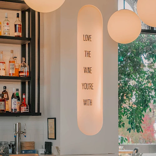 A stylish bar scene with large globe lights, a marble counter, and a vertical neon sign reading &ldquo;LOVE THE WINE YOU&rsquo;RE WITH&rdquo; ending this sentence.