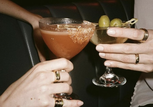 A group of people clinking glasses of beer in a celebratory toast, with warm lighting and a festive atmosphere.