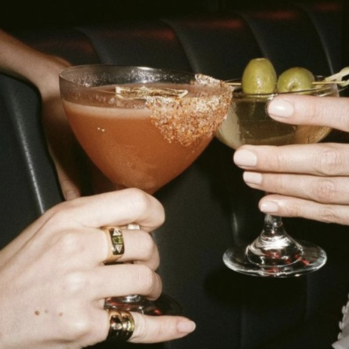 A group of people clinking glasses of beer in a celebratory toast, with warm lighting and a festive atmosphere.
