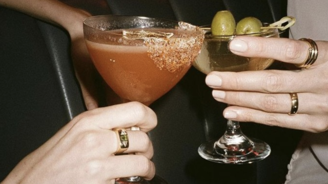 A group of people clinking glasses of beer in a celebratory toast, with warm lighting and a festive atmosphere.