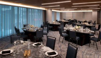 The image shows an elegantly set banquet hall with round tables, black chairs, and place settings, ready for an event or dinner.