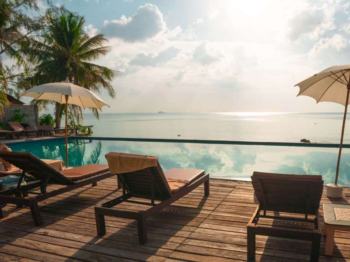 A serene beach scene with lounge chairs, umbrellas, palm trees, and a calm sea reflecting the sky, creating a relaxing atmosphere.