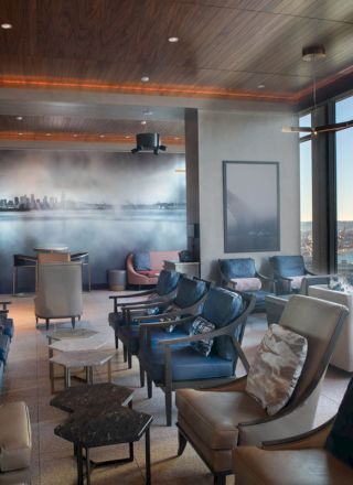 A modern lounge with stylish seating, large windows, and an artwork of a bridge on the wall, offering a scenic view outside.