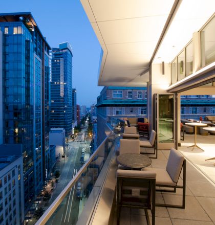 A modern rooftop terrace with seating overlooks a cityscape of tall buildings at dusk, creating a serene urban atmosphere.