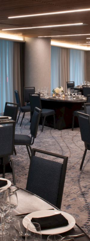 The image shows an elegant banquet room with round tables set for dining, featuring black chairs and tableware, and dim ambient lighting.