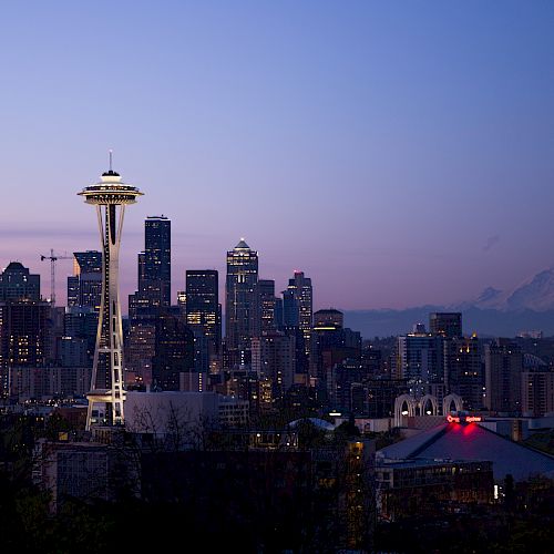 A cityscape at dusk with a prominent tower and mountains in the background under a twilight sky.