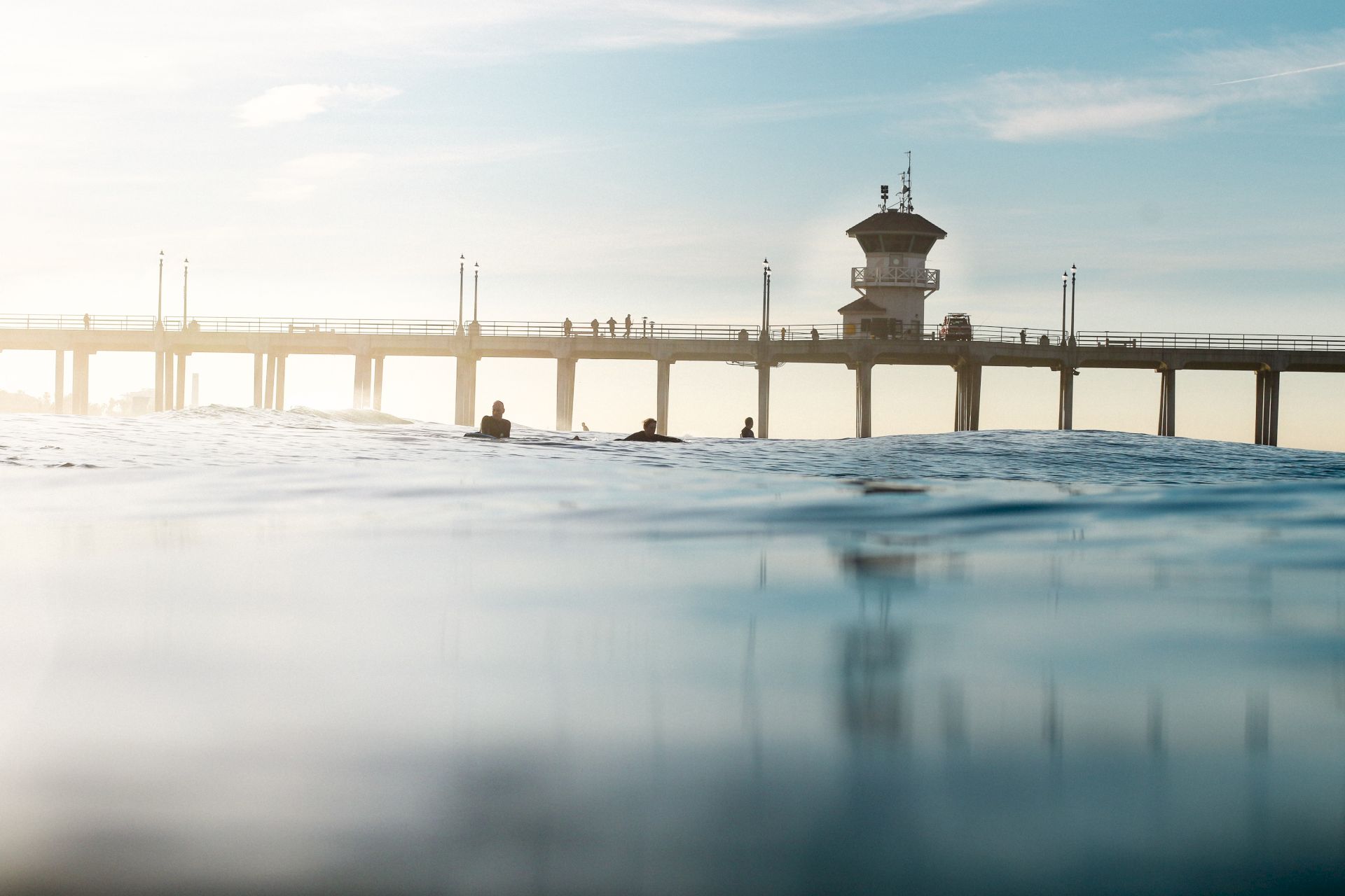 A serene view of a pier extending over the water with a few people visible on it, under a clear sky.